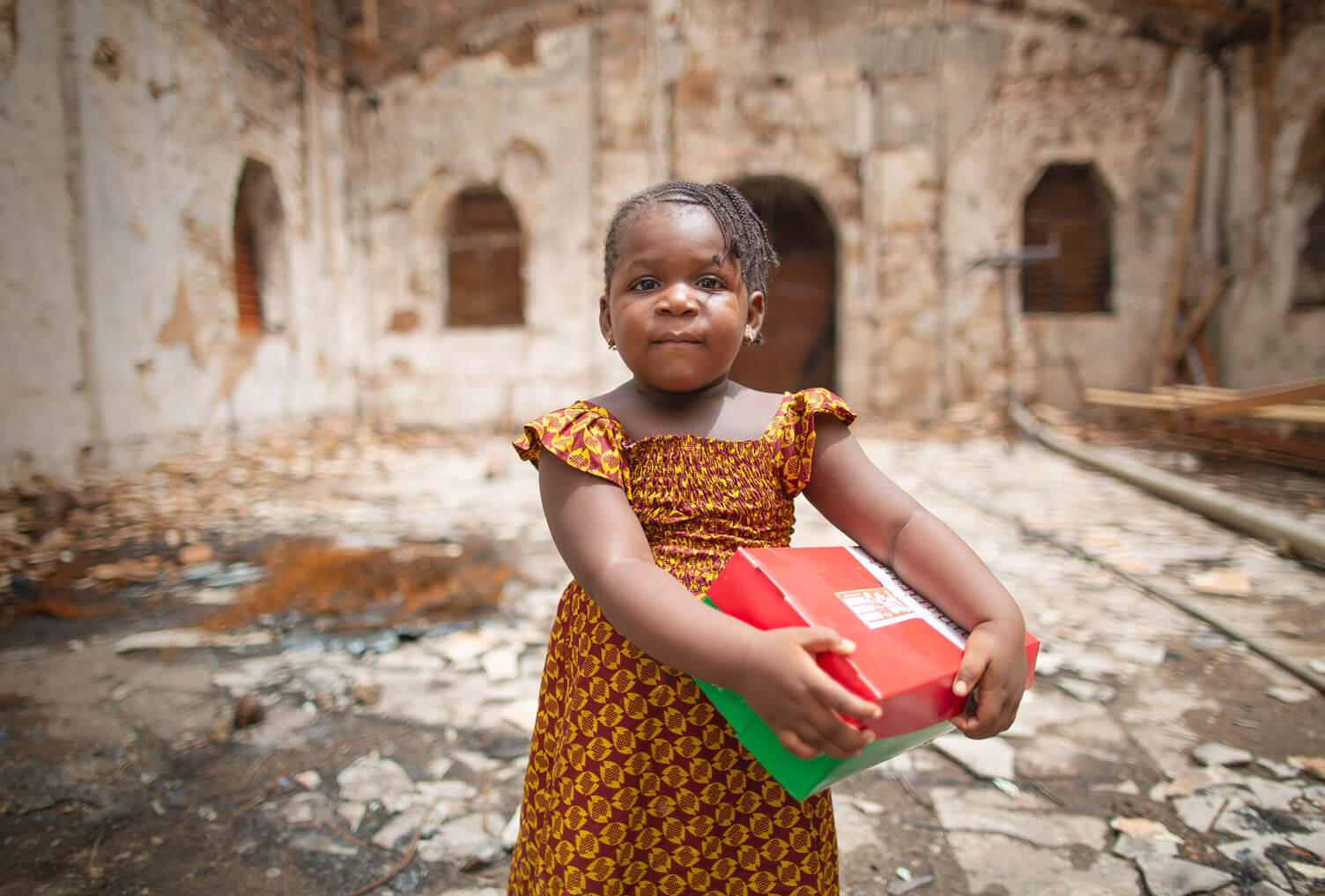 a young girl holds an Operation Christmas Child shoebox while standing inside of a burned church