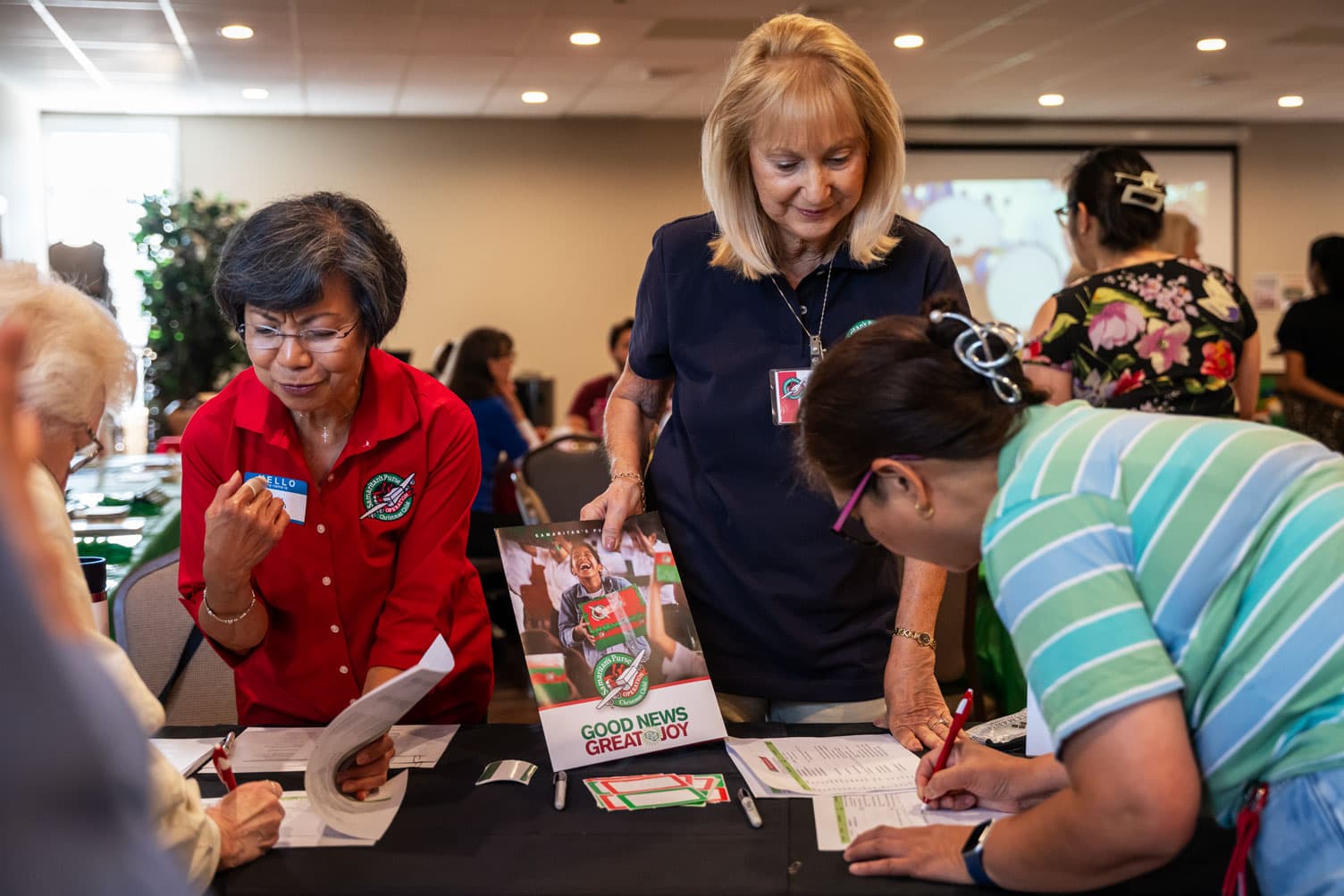 Two female Operation Christmas Child volunteers assisting workshop attendees with sign-in