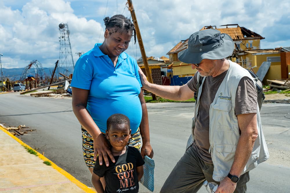 Samaritan’s Purse worker prays with a Jamaican woman and child amid storm-damaged homes after Hurricane Melissa.