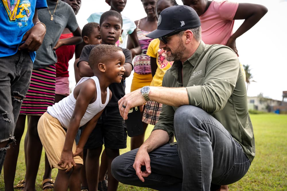 Graham connects with a group of local children in Jamaica, eventually breaking into laughter at the young boy’s energetic expressions.