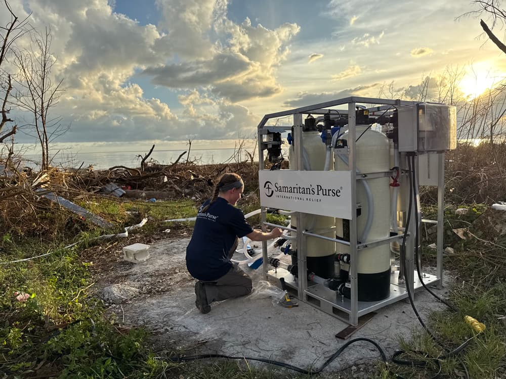 Samaritan’s Purse staff member kneels beside water purification equipment, connecting hoses at sunset in Jamaica.
