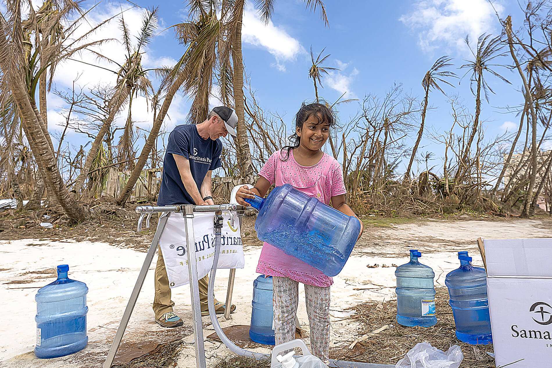 a volunteer helping a girl in Saipan fill up a large water jug