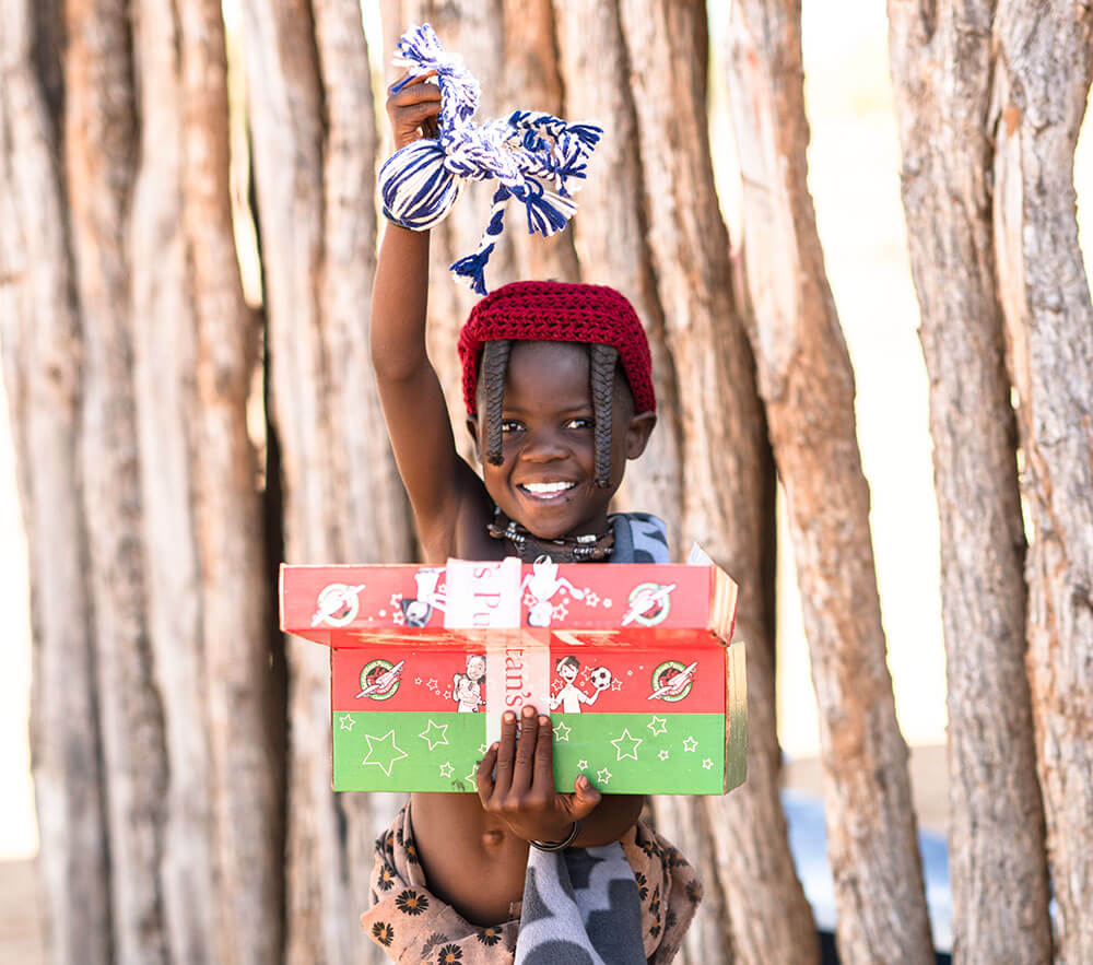 A smiling child from the Himba tribe holding their Operation Christmas Child shoebox.