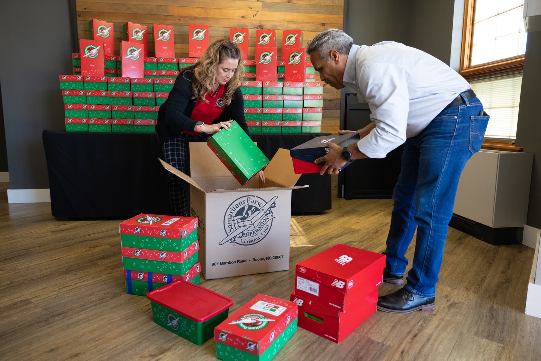 Two volunteers, a male and female, loading individual shoeboxes into and larger Operation Christmas Child box