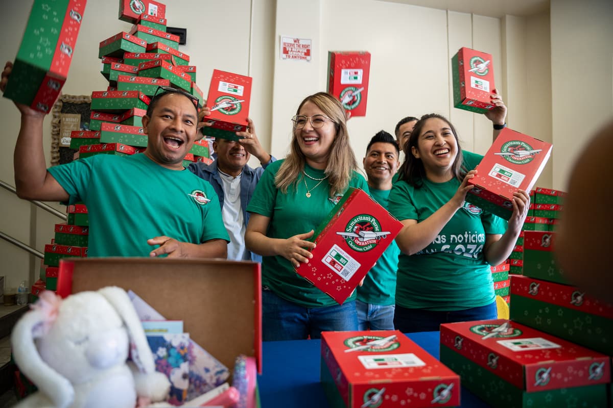 Group of volunteers and leaders excitedly holding up Operation Christmas Child shoeboxes at a collection event