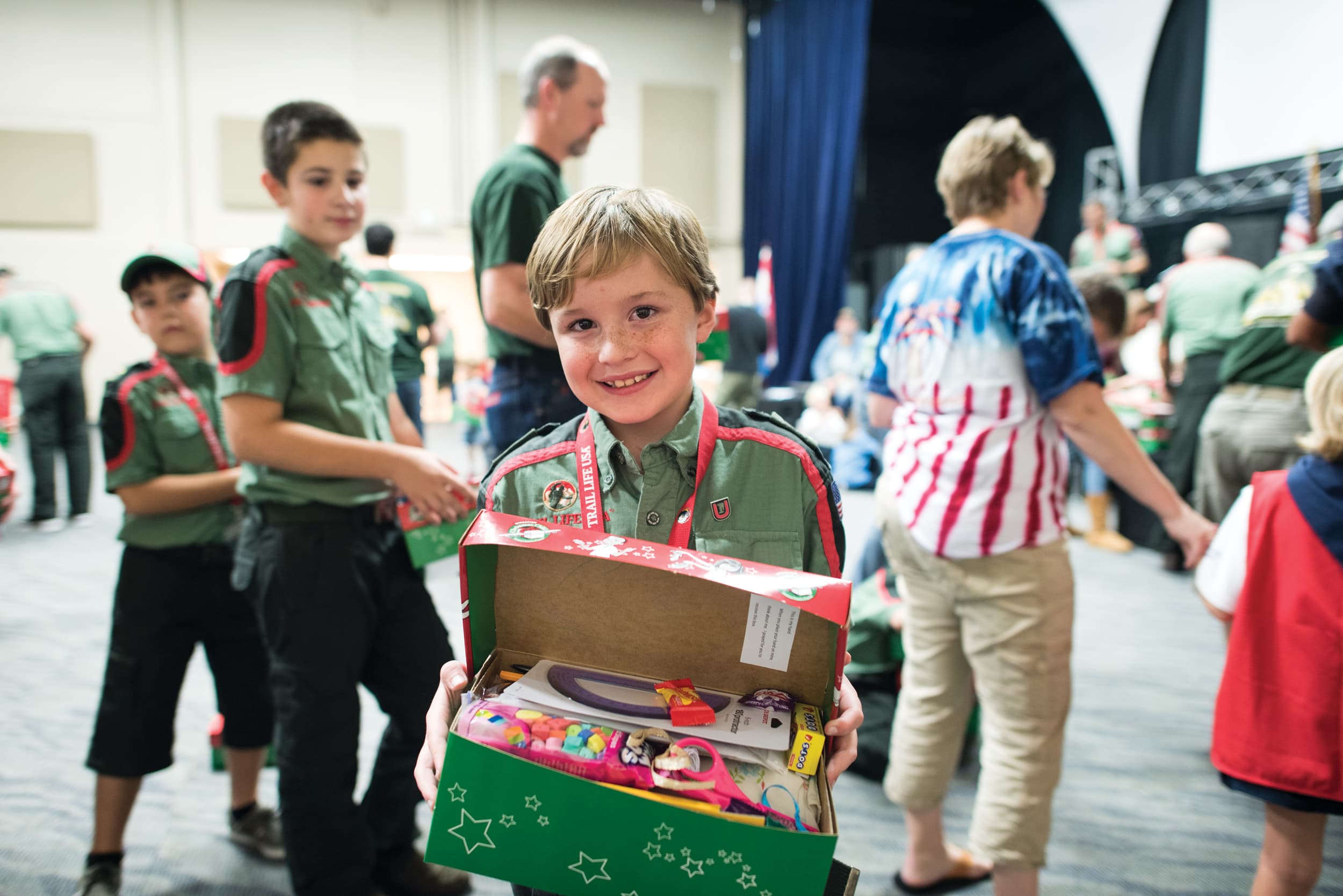 Young boy in a Trail Life uniform holding an open shoebox full of gifts and treats