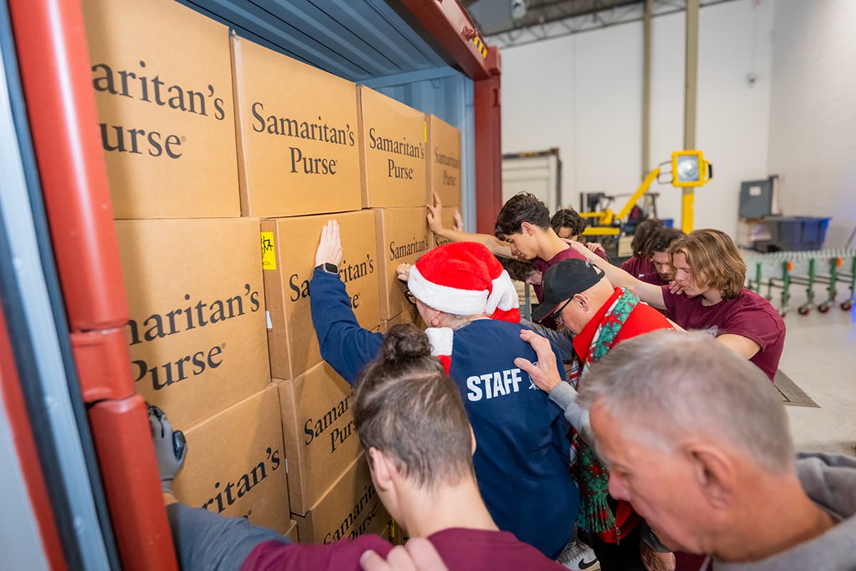 Group of Operation Christmas Child staff praying while laying hands on boxes packed in the back of a transport truck