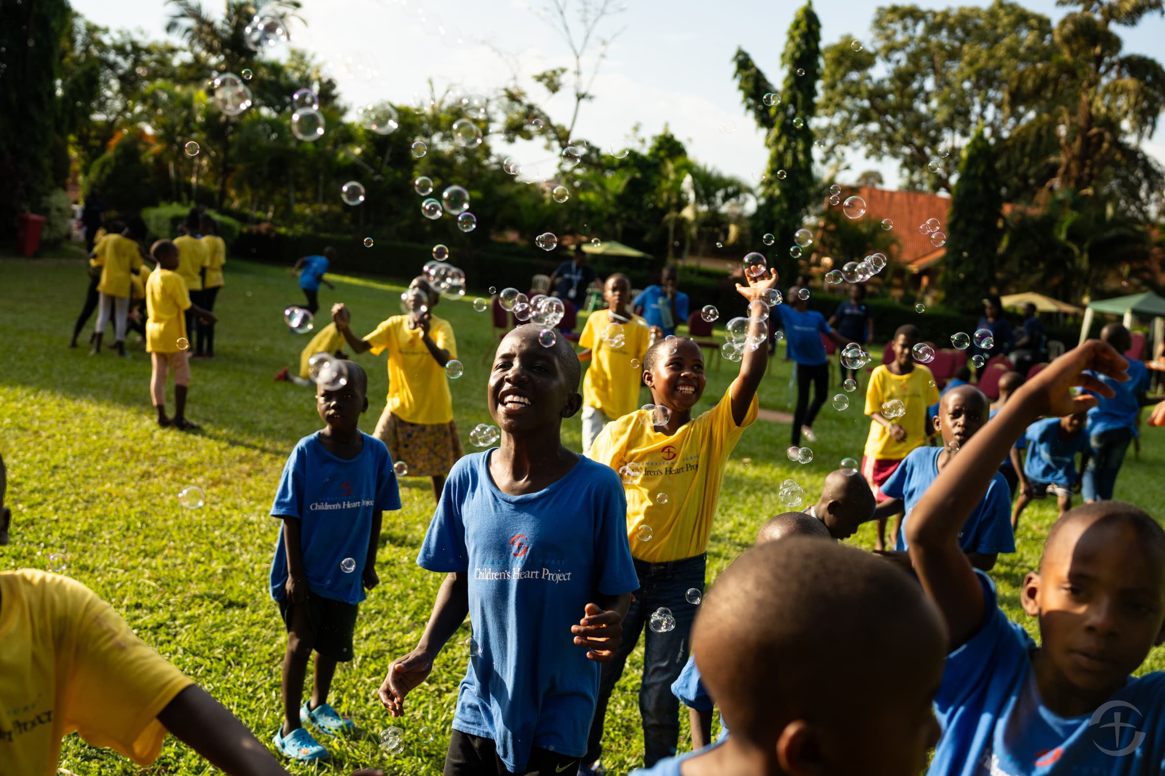 Excited and laughing children surrounded by floating bubbles at a Children's Heart Project Camp in Uganda